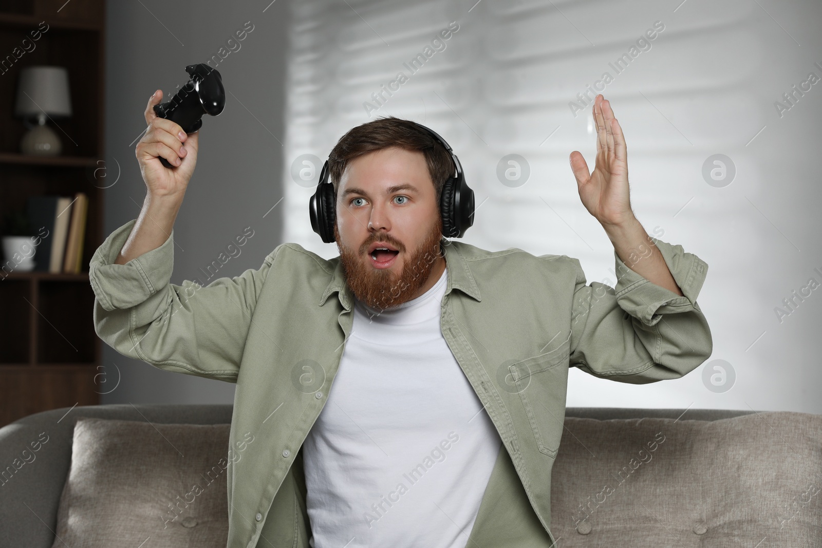 Photo of Surprised man in headphones with game controller at home