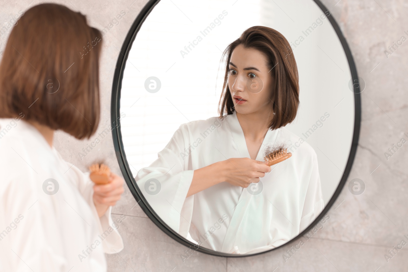 Photo of Young woman with hair loss problem looking at mirror indoors