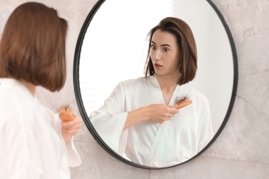 Photo of Young woman with hair loss problem looking at mirror indoors