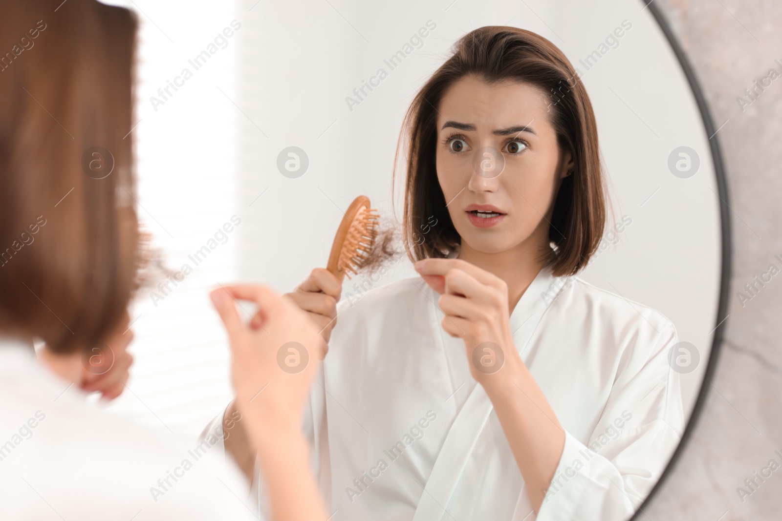 Photo of Emotional woman taking her lost hair from brush in bathroom. Alopecia problem