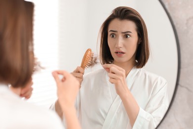 Emotional woman taking her lost hair from brush in bathroom. Alopecia problem