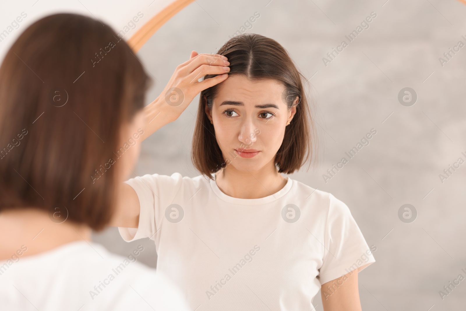 Photo of Sad woman with hair loss problem looking at mirror indoors