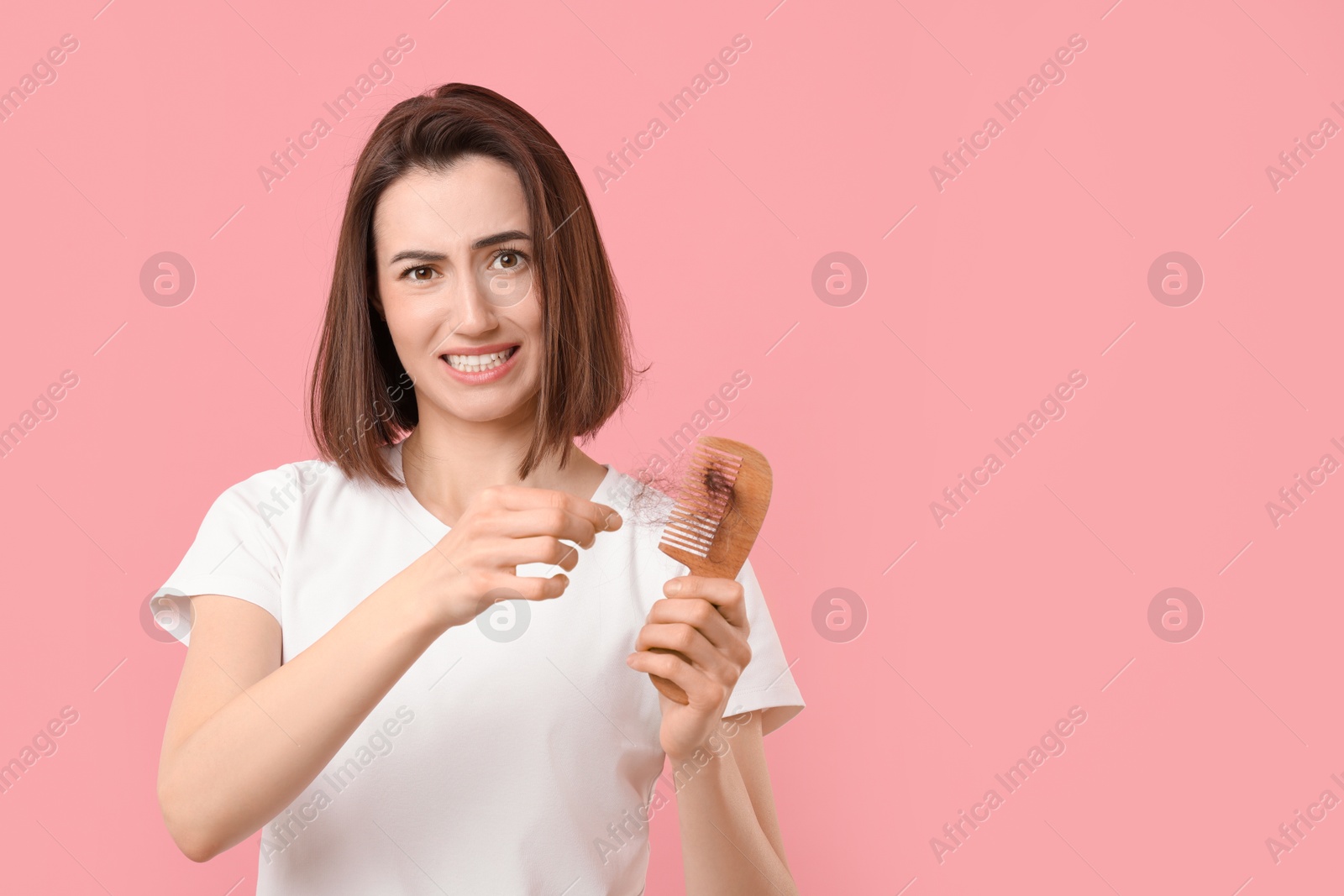 Photo of Emotional woman taking her lost hair from comb on pink background, space for text. Alopecia problem