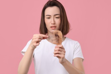 Stressed woman taking her lost hair from comb on pink background. Alopecia problem