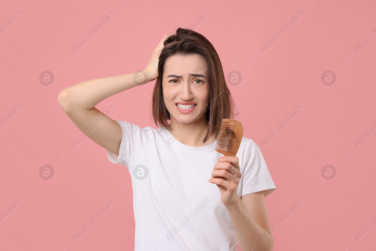 Photo of Emotional woman holding comb with lost hair on pink background. Alopecia problem