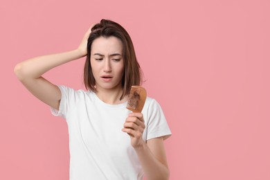 Photo of Sad woman holding comb with lost hair on pink background, space for text. Alopecia problem