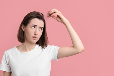 Young woman suffering from hair loss problem on pink background. Space for text