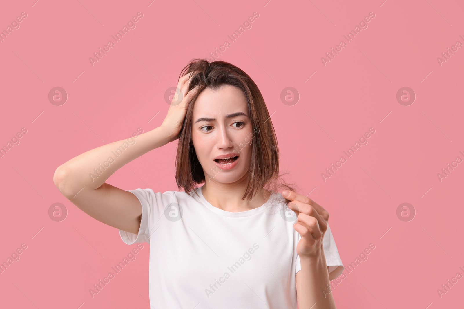 Photo of Emotional woman holding clump of lost hair on pink background. Alopecia problem