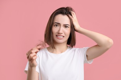 Photo of Emotional woman holding clump of lost hair on pink background. Alopecia problem