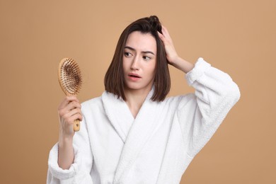 Photo of Stressed woman holding brush with lost hair on light brown background. Alopecia problem