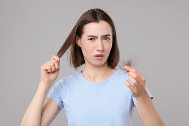 Photo of Sad woman holding clump of lost hair on grey background. Alopecia problem