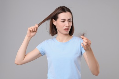 Sad woman holding clump of lost hair on grey background. Alopecia problem