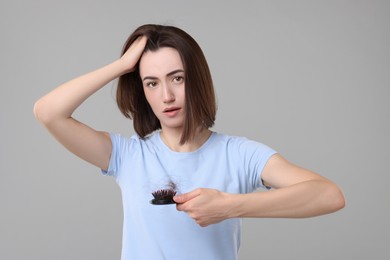 Photo of Stressed woman holding brush with lost hair on grey background. Alopecia problem