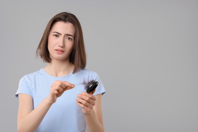 Sad woman taking her lost hair from brush on grey background, space for text. Alopecia problem