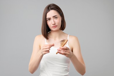 Photo of Sad woman taking her lost hair from brush on grey background. Alopecia problem