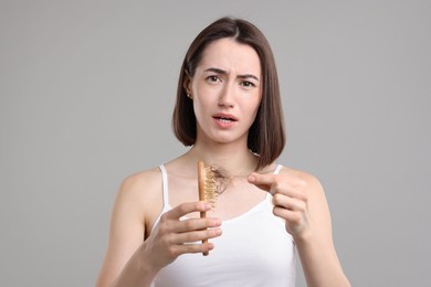 Stressed woman taking her lost hair from brush on grey background. Alopecia problem