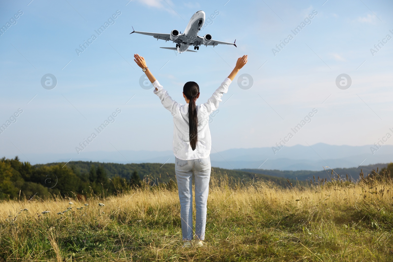 Image of Woman looking at airplane flying in sky over mountains, back view