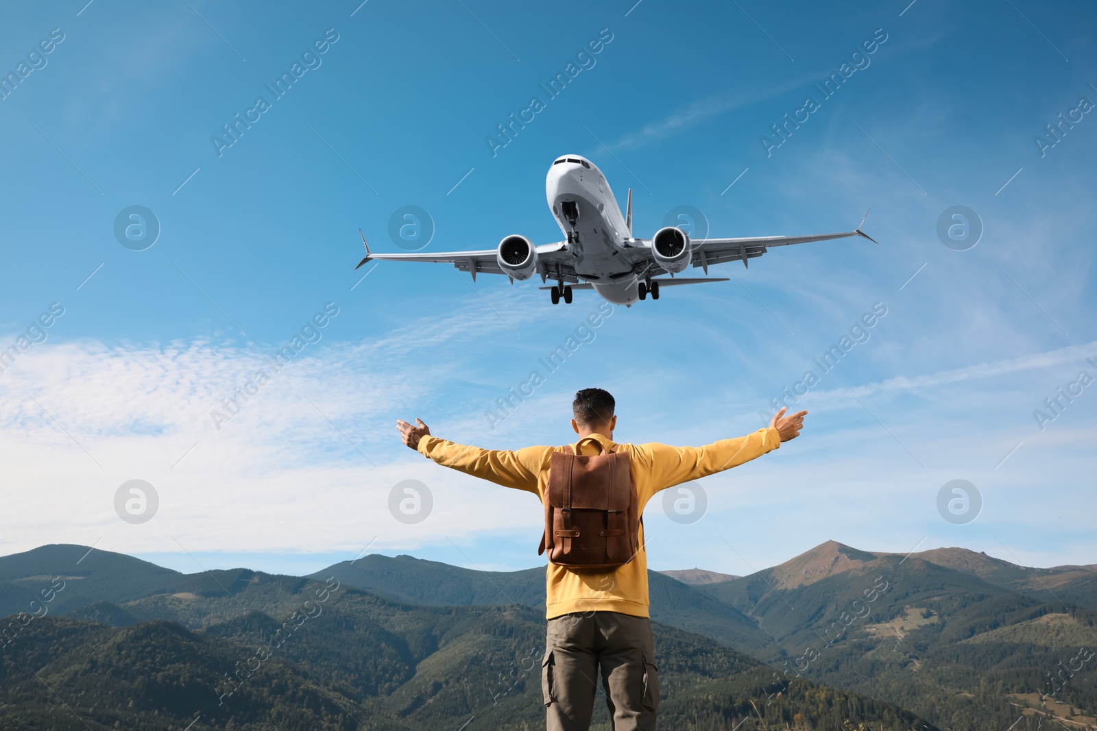 Image of Man looking at airplane flying in sky over mountains, back view