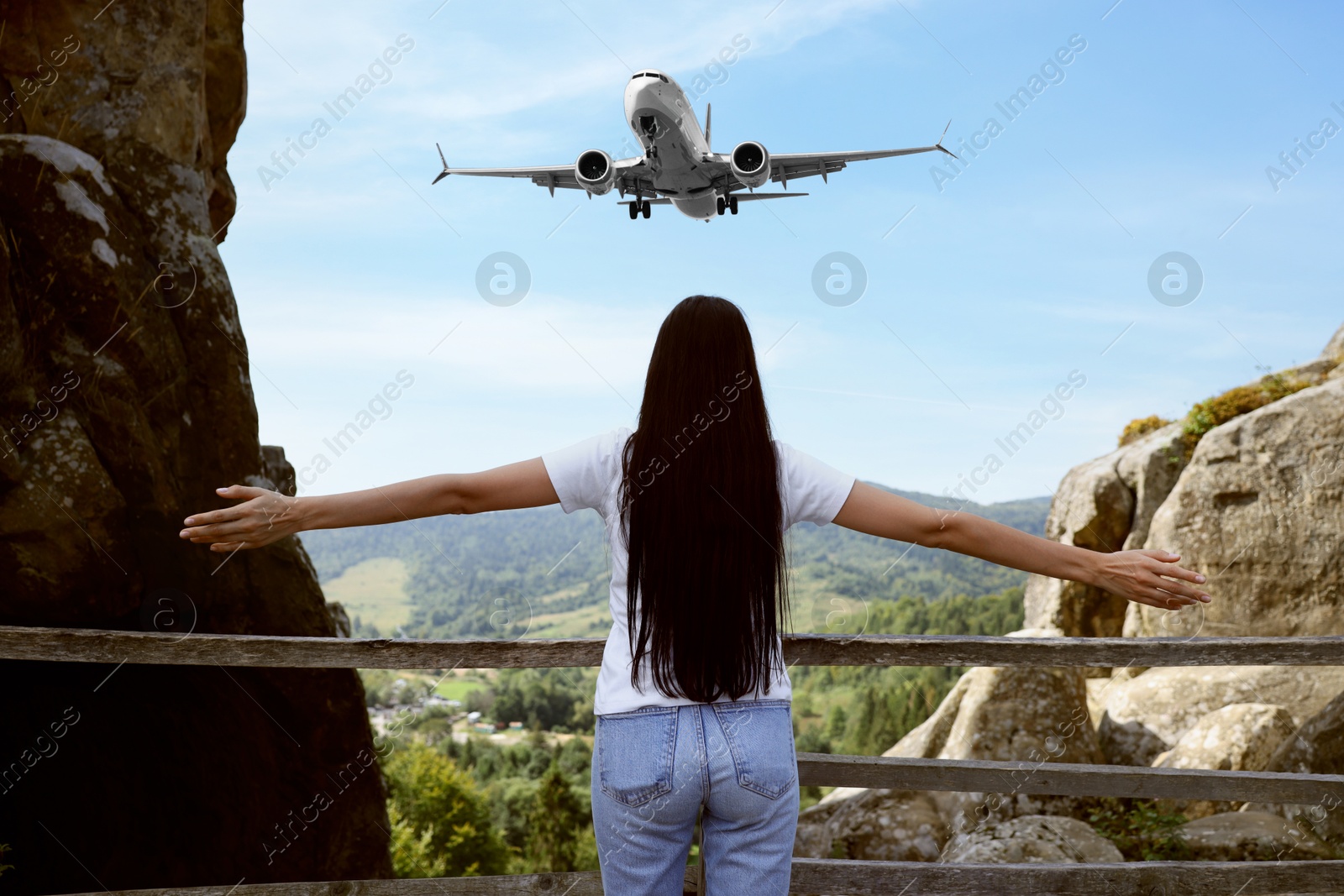 Image of Woman looking at airplane flying in sky over mountains, back view