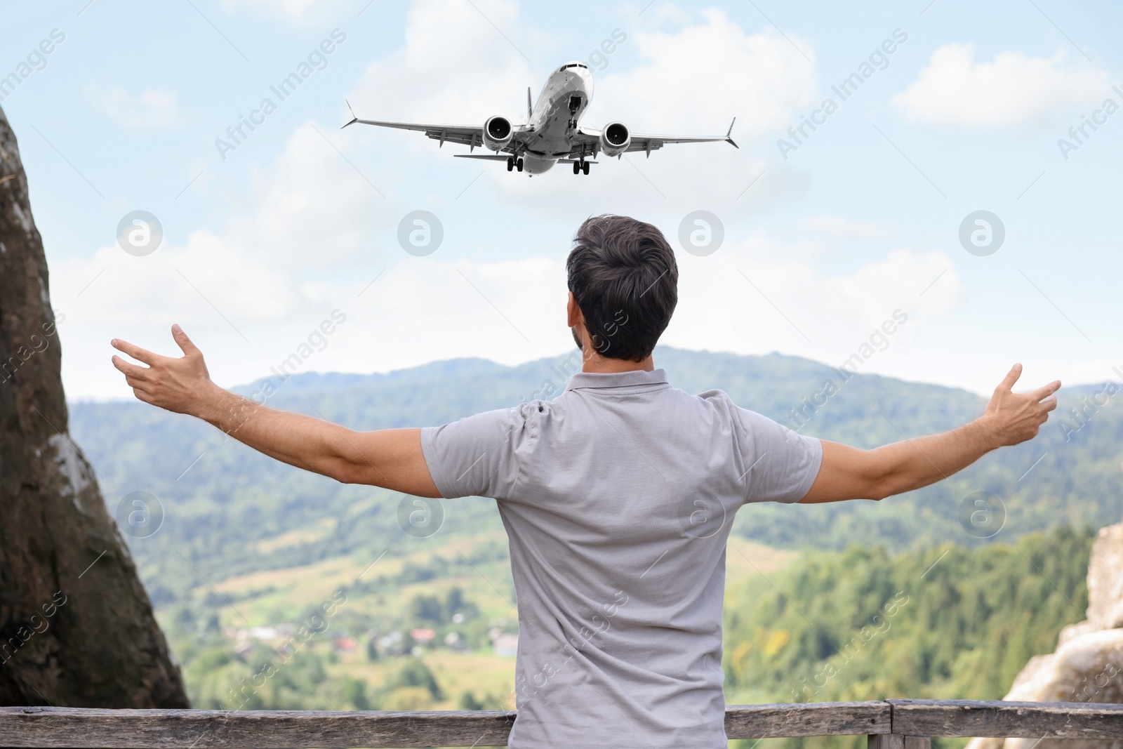 Image of Man looking at airplane flying in sky over mountains, back view