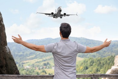 Man looking at airplane flying in sky over mountains, back view