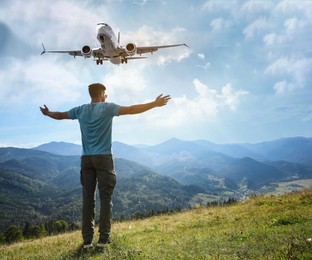 Man looking at airplane flying in sky over mountains, back view