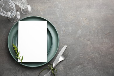 Empty menu, plates, cutlery, glasses and floral decor on grey table, top view. Mockup for design