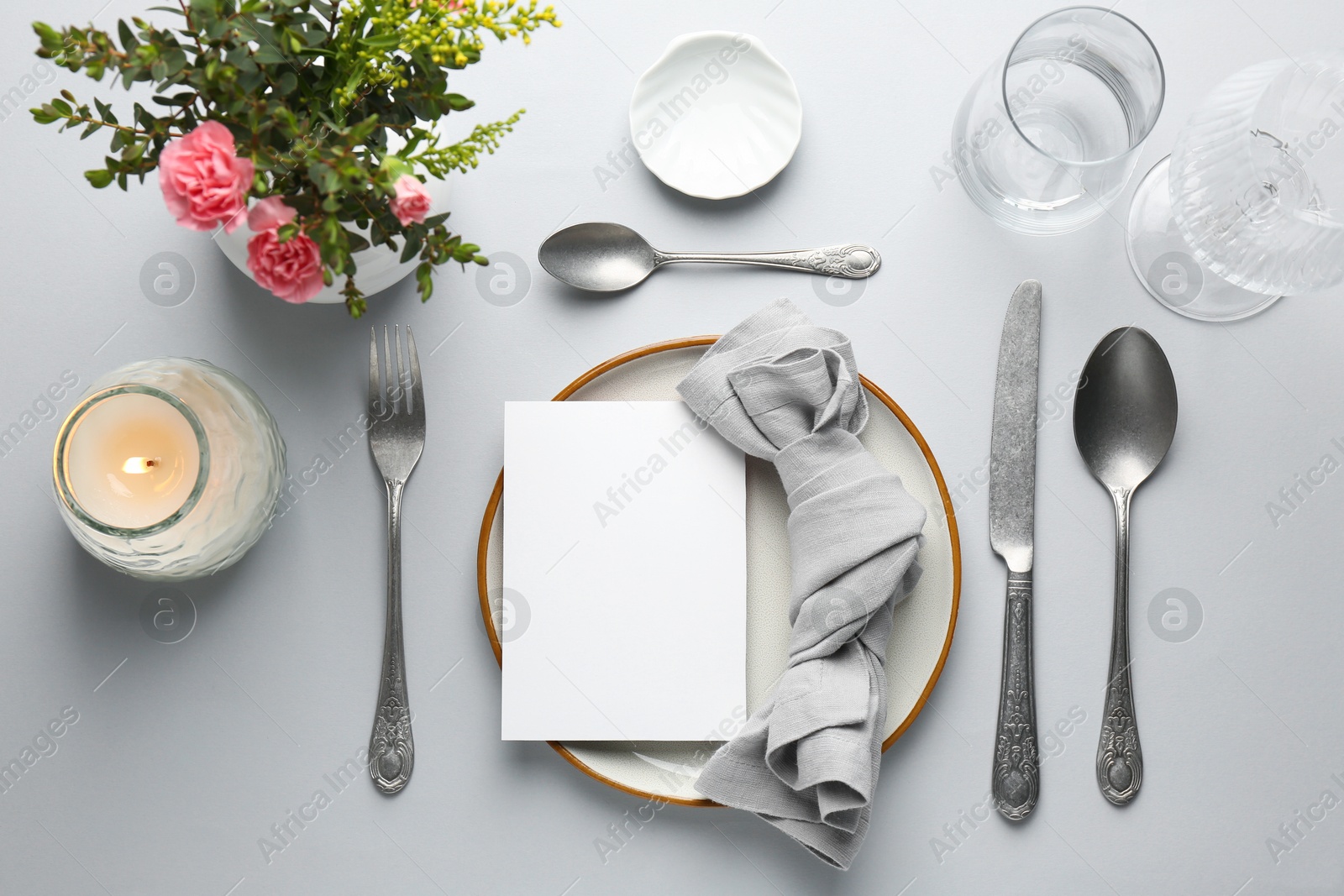 Photo of Empty menu, tableware, candle and floral decor on light grey table, flat lay. Mockup for design