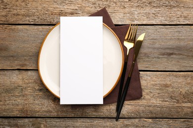 Photo of Empty menu, cutlery, plate and napkin on wooden table, top view. Mockup for design