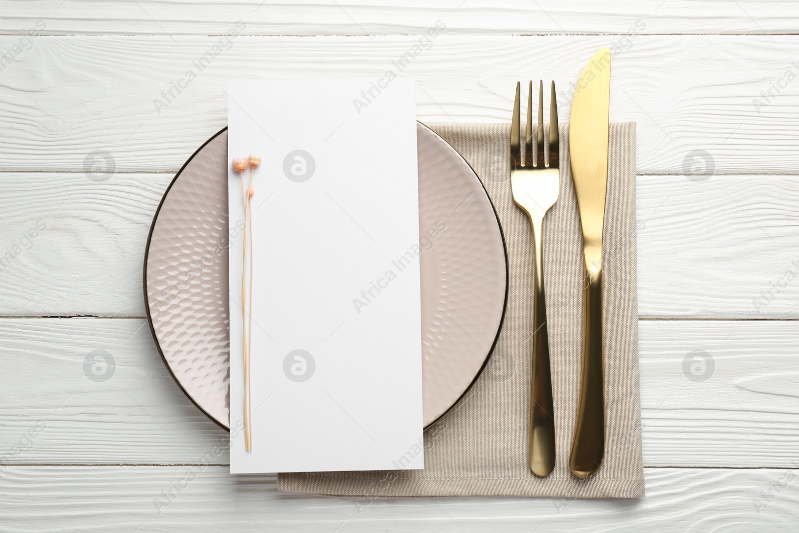 Photo of Empty menu, cutlery, plate, napkin and floral decor on white wooden table, top view. Mockup for design