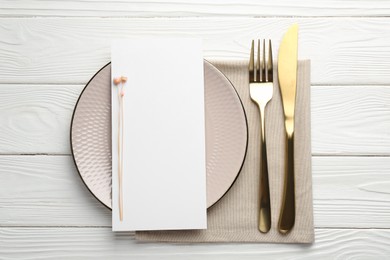 Photo of Empty menu, cutlery, plate, napkin and floral decor on white wooden table, top view. Mockup for design