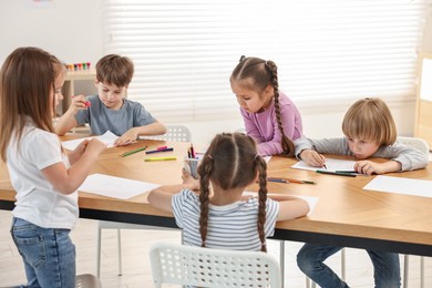 Group of children drawing at wooden table indoors