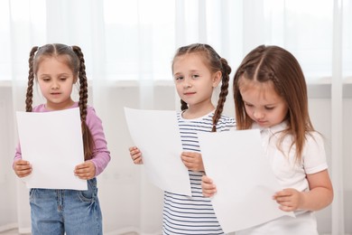 Photo of Cute little children with sheets of paper singing indoors