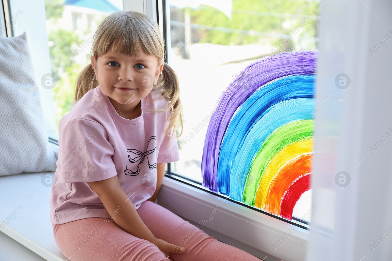 Photo of Little girl near rainbow painting on window indoors