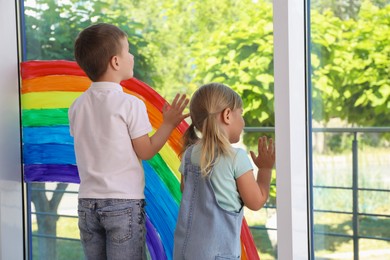Children touching picture of rainbow on window indoors