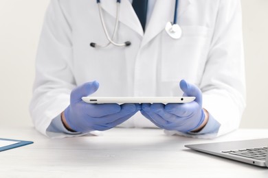 Photo of Doctor with tablet at white wooden table, closeup