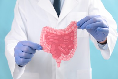 Photo of Doctor with paper intestine cutout on light blue background, selective focus