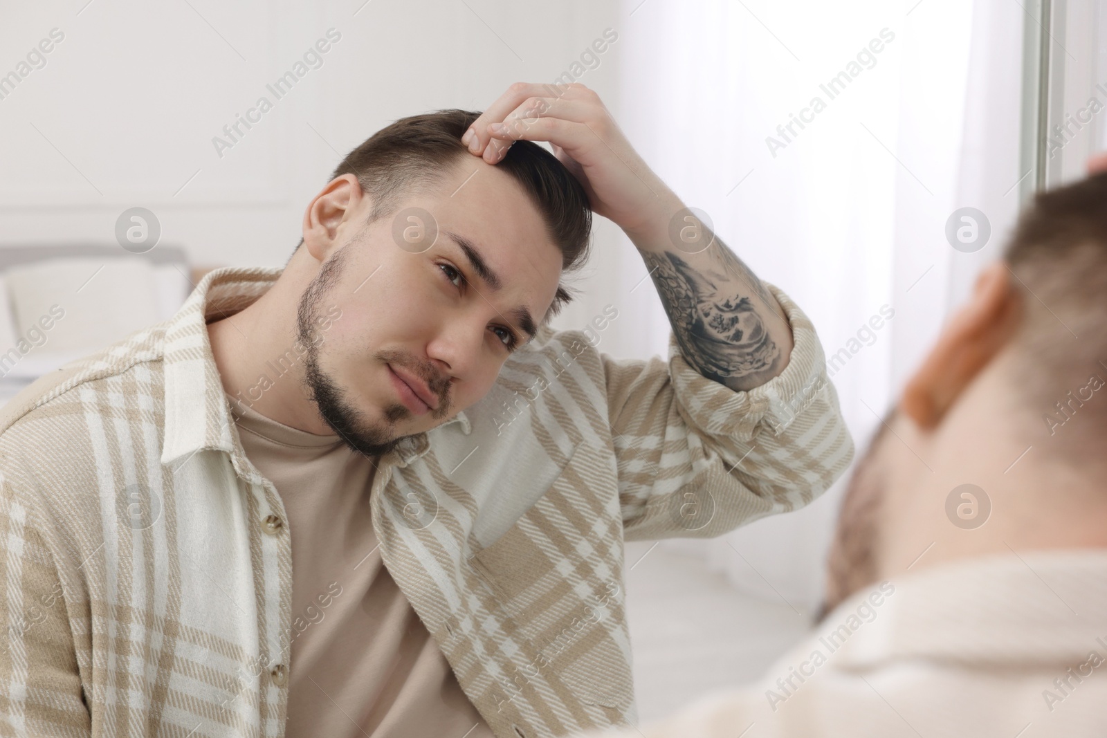 Photo of Baldness concept. Sad man with receding hairline looking at mirror indoors