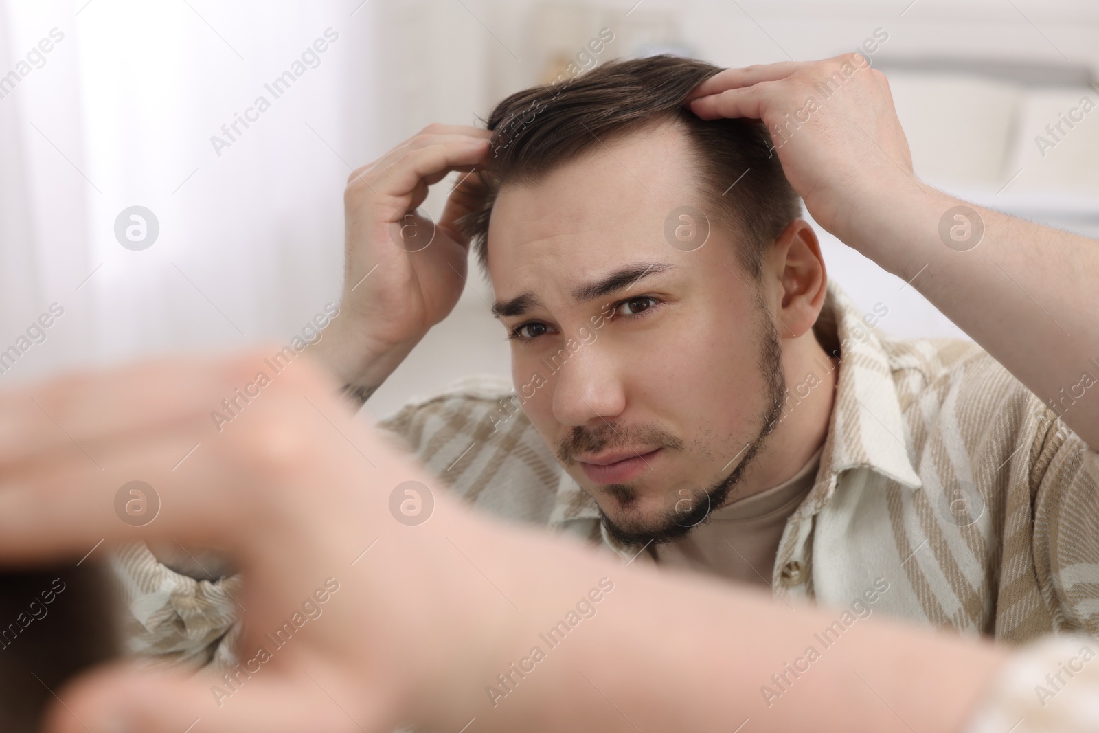 Photo of Baldness concept. Sad man with receding hairline looking at mirror indoors