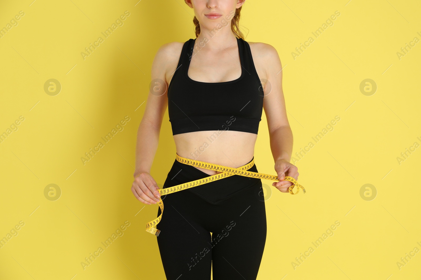 Photo of Woman with measuring tape showing her slim body against yellow background, closeup