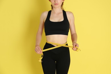 Woman with measuring tape showing her slim body against yellow background, closeup