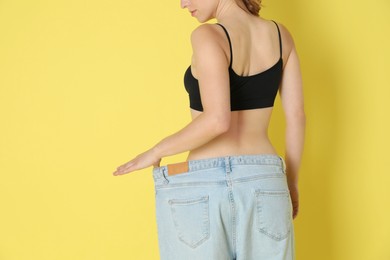 Photo of Woman in big jeans showing her slim body on yellow background, closeup. Space for text