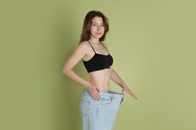 Photo of Woman in big jeans showing her slim body on olive background