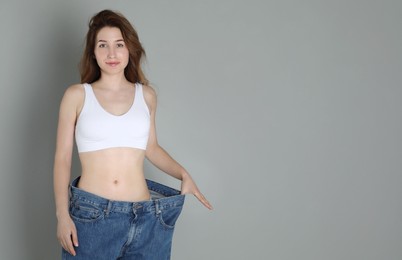 Woman in big jeans showing her slim body on grey background, space for text