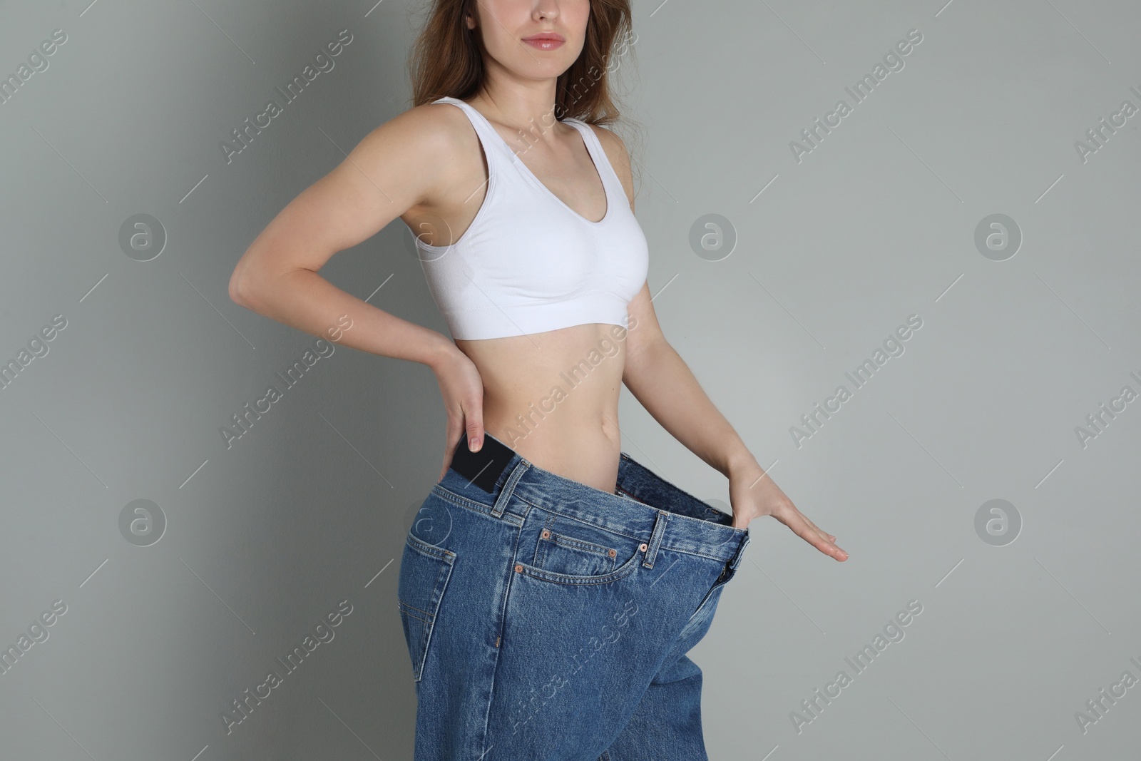 Photo of Woman in big jeans showing her slim body on grey background, closeup