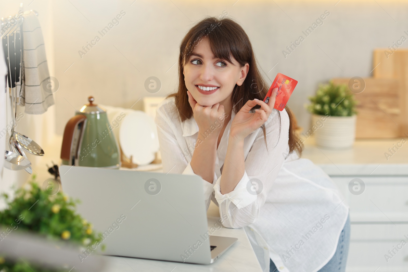 Photo of Online banking. Smiling woman with credit card and laptop paying purchase in kitchen