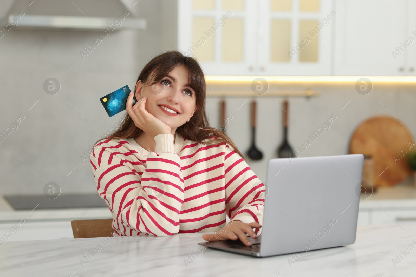 Photo of Online banking. Smiling woman with credit card and laptop paying purchase at table indoors