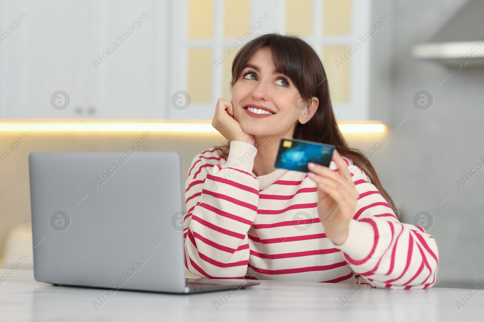 Photo of Online banking. Smiling woman with credit card and laptop paying purchase at table indoors