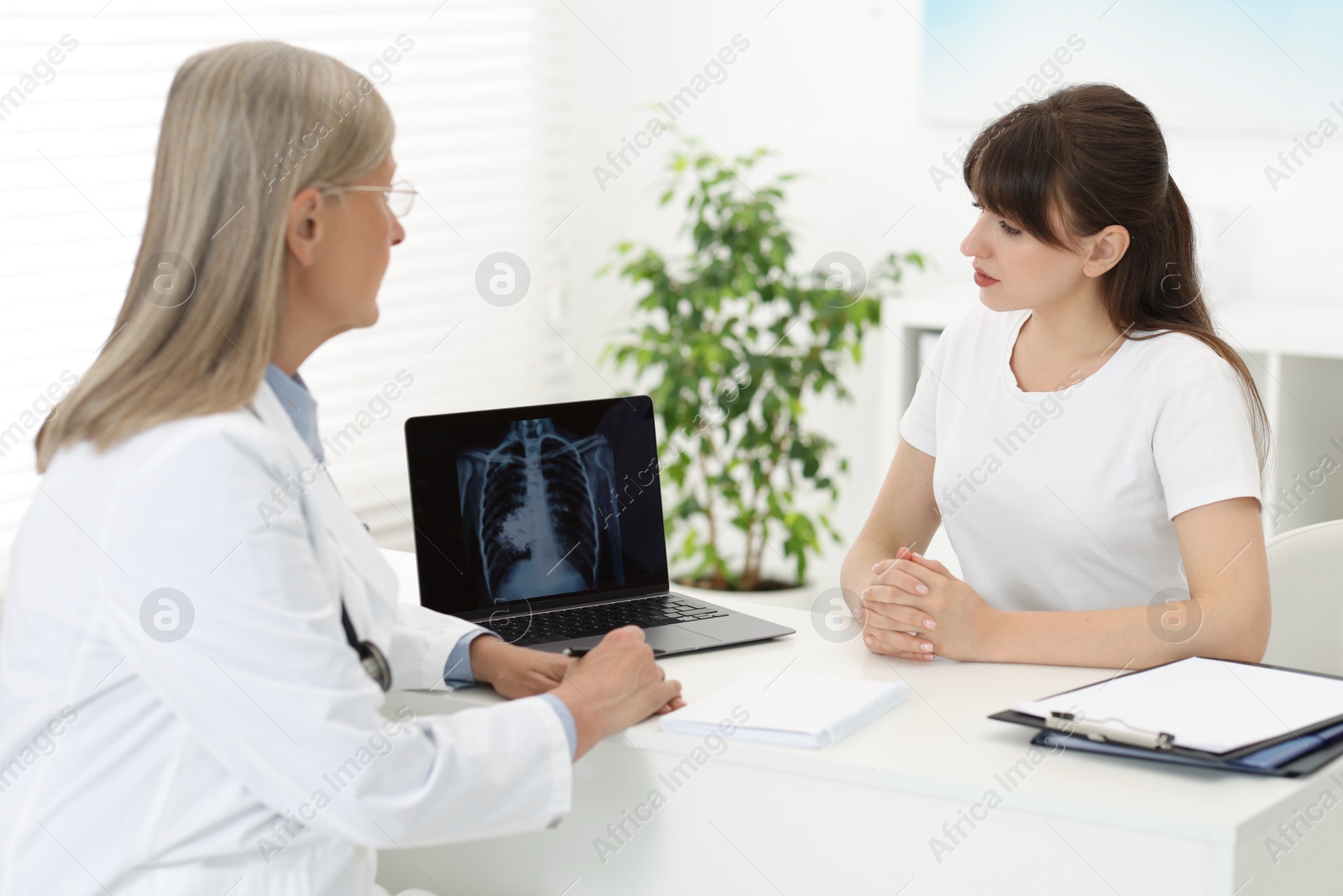 Photo of Lung cancer. Doctor showing chest x-ray on laptop to her patient in clinic