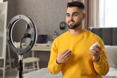 Beauty blogger reviewing cosmetic product and recording video with smartphone and ring lamp at home